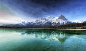 藍天下，白雪覆蓋的山峰倒映在綠松石色的湖泊中。 — 雪山 壁紙