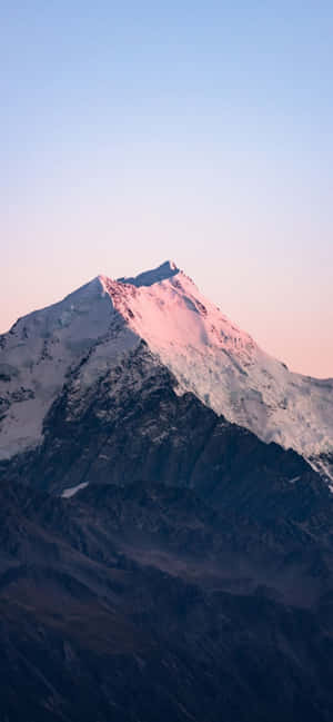 白雪覆蓋的山峰沐浴在粉紅色的日出光芒中。 — 自然 iPhone 壁紙