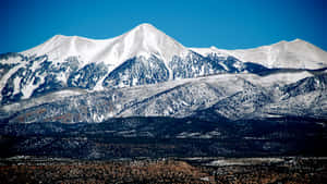 晴朗藍天下白雪覆蓋的山脈，下方是崎嶇的山谷。 — 冬季桌面 壁紙