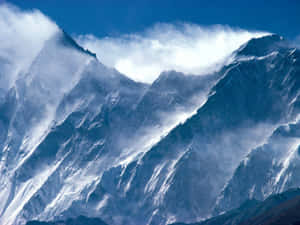 在晴朗的藍天下，白雪覆蓋的山峰聳立於雲層之上。 — 山脈 壁紙