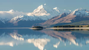 白雪皚皚的山峰倒映在平靜的藍色湖面上，天空晴朗。 — 5120x2880 壁紙