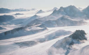白雪覆蓋的山峰在廣闊的阿爾卑斯山景中，聳立於旋轉的迷霧之上。 — 南極洲 壁紙
