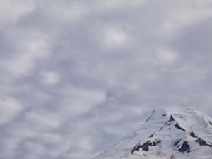 陰天時白雪覆蓋的山峰從灰色雲層中升起。 — 海景 壁紙