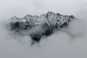 白雪覆蓋的山峰在陰天中高聳於雲海之上。 — 寒冷 壁紙