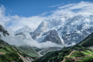 白雪覆蓋的山脈聳立在綠色山谷之上，有梯田和蜿蜒的道路。 — MacBook Air M2 壁紙