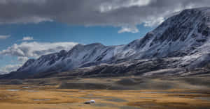 白雪覆蓋的山峰聳立於金色平原之上，天空陰雲，有一座氈帳。 — 秋季 壁紙