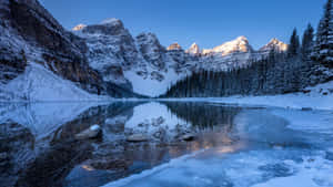 結冰的湖面在日出時分倒映著白雪覆蓋的山脈。 — 加拿大 壁紙