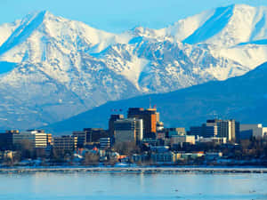冬季城市天際線，有白雪覆蓋的山脈和平靜水面。 — 城市風景 壁紙