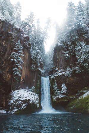 白雪覆蓋的瀑布流經森林峽谷，有常青樹和霧氣。 — POCO Pad 壁紙