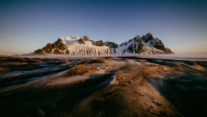 黑沙灘後方的雪山，伴隨著霧氣和金色光線。 — 冬季風景 壁紙