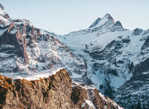 白雪覆蓋的山峰，岩石上有一座小木屋。 — 雪景 GIF 壁紙