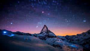 白雪覆蓋的山峰在星空暮色下聳立，下方有閃爍的燈光。 — 藍色銀河 壁紙