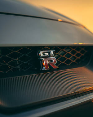 碳纖維格柵上GT-R汽車徽章沐浴在金色夕陽光中。 — 日產 壁紙