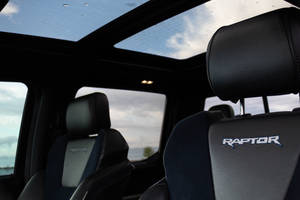 卡車內黑色皮革座椅帶 Raptor 標誌，天窗顯示多雲天空。