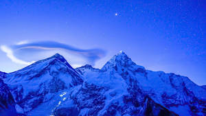 在繁星點點的夜空下，積雪的山脈伴隨著發光的透鏡狀雲。 — 丘陵景觀 壁紙