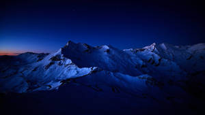 暮色中積雪的山脈，下方有一條蜿蜒的道路，星空點綴。 — 美麗的夜晚 壁紙