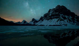 在繁星點點的夜空下，積雪的山峰倒映在湖中，銀河清晰可見。 — 加拿大 壁紙
