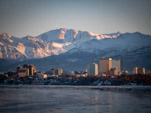 城市天際線與積雪的山峰在日出時倒映在結冰的河流中。 — 城市風景 壁紙