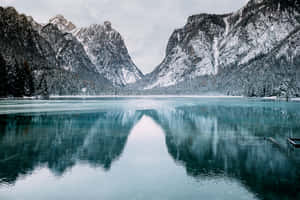 積雪的山峰倒映在灰色天空下平靜的碧綠湖水中。 — 冬季風景 壁紙