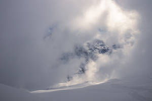 積雪的山峰穿破雲層，前景有滑雪痕跡。 — 白雪公主 壁紙