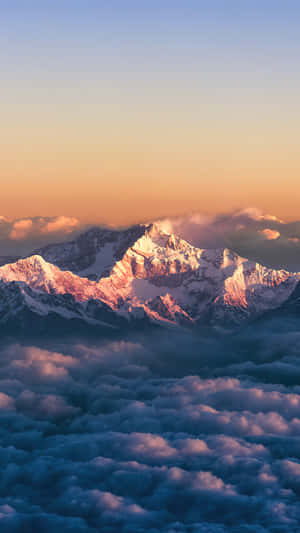 積雪的山脈在日出時升起於雲層之上，呈現金色和藍色色調。 — 美學天空 壁紙