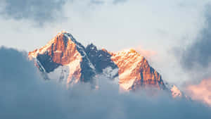 日出時從雲層中浮現的積雪山峰 — 山脈 壁紙