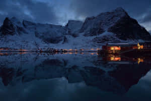 積雪的山峰和木屋在平靜的水面上倒映，黃昏時分。 — 冬季風景 壁紙
