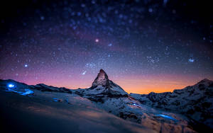 星空暮色天空下的積雪山峰，下方有發光的藍色燈光 — 冬季風景 壁紙