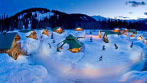 積雪的小屋亮著溫暖的燈光，坐落在暮色中的山林裡。 — 可愛聖誕節 壁紙