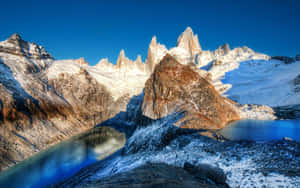 積雪的山峰在清澈的藍天下倒映在綠松石色的湖中。 — 2880x1800 壁紙
