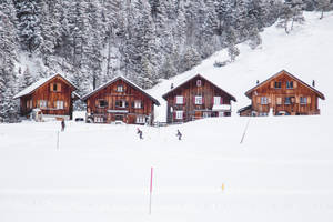 滑雪者在積雪的山村中滑過木製小木屋。 — 冬季房屋 壁紙