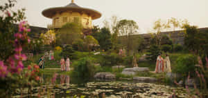 穿著傳統長袍的人們走過一個有金色寶塔和百合池塘的茂盛花園。 — 木蘭 壁紙