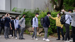 穿著校服和口罩的學生在學校外行走，老師向他們打招呼。 — 精細 壁紙