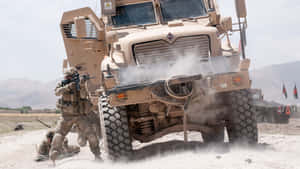 士兵在塵土飛揚的沙漠景觀中靠近一輛裝甲軍用卡車移動。 — 美國陸軍 GIF 壁紙