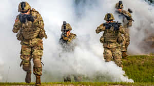 穿著迷彩裝備的士兵在草地上穿過煙霧移動。 — 第七班 壁紙