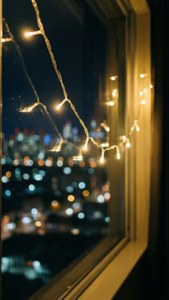 串燈在窗邊溫暖地發光，俯瞰夜間模糊的城市。 — 聖誕美學 壁紙