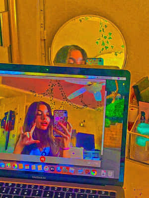 在裝飾過的房間裡，筆記型電腦螢幕上有人在鏡子和藤蔓旁自拍。 — 另類美學 壁紙