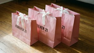 三個粉紅色的Forever 21袋子，搭配白色緞帶，放在木地板上。 — 永遠21 壁紙