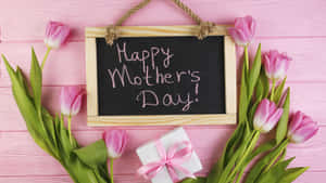 粉紅色鬱金香和禮物盒圍繞著一塊帶有「Happy Mother's Day」訊息的黑板。 — 2560x1440 壁紙