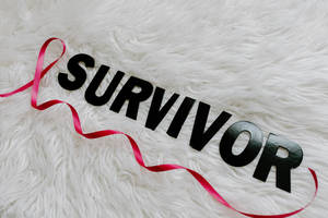 黑色 'SURVIVOR' 字母配紅色絲帶，背景為白色絨毛。 — 粉紅色 壁紙