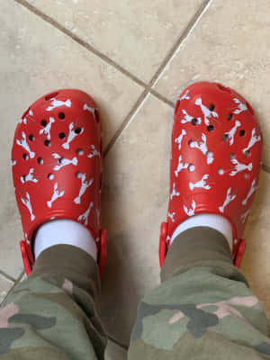 米色瓷磚地板上的紅色Crocs鞋，帶有白色龍蝦圖案，搭配迷彩褲和白色襪子。 — iPad 第9代 壁紙