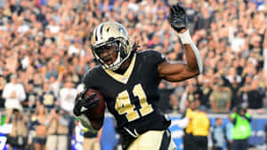 身穿聖徒隊制服的美式足球員帶著球奔跑並舉手慶祝。 — Alvin Kamara 壁紙