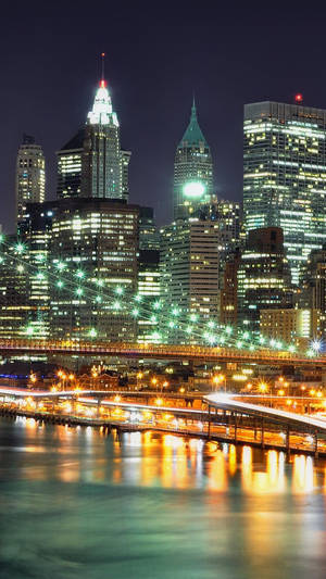 紐約天際線的夜景，建築物燈火通明，橋樑橫跨水面。 — 城市燈光 壁紙