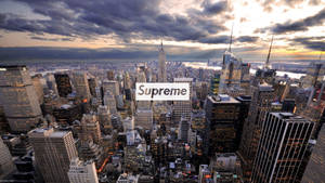 紐約市天際線在黃昏時，雲層和燈火通明的摩天大樓上疊加著Supreme標誌。 — 紐約 壁紙