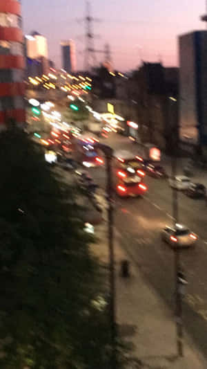 黃昏時模糊的城市街景，有移動的汽車和明亮的燈光。 — 霓虹車 壁紙