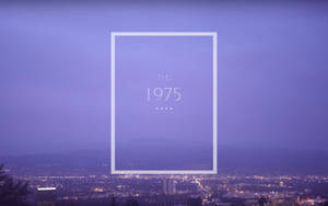 一個帶框的文字疊加層，在紫色黃昏城市天際線背景下顯示「THE 1975」。 — 1975樂團 壁紙