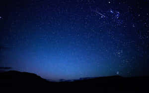 一顆流星劃過繁星點點的夜空，在黑暗的山巒剪影之上。 — 美學深藍 壁紙