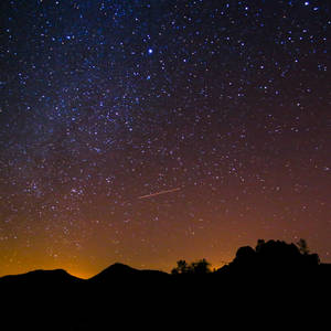 一顆流星劃過繁星點點的夜空，上方是黑暗的山脈輪廓。 — 夜空 壁紙