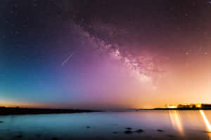繁星點點的夜空，流星劃過平靜的湖面，倒映著遠處的燈光和銀河 — 3:2 壁紙