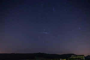 繁星點點的夜空，流星軌跡劃過山丘和房子上方。 — MacBook Air M2 壁紙